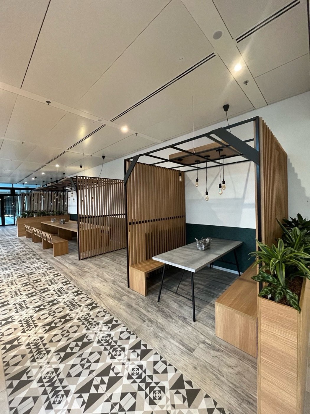 Seating pergolas made of slatted oak and steel with pendant lights and planters