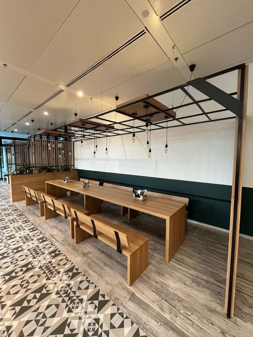 Long oak tables with benches under the steel pergola with filament pendant lights